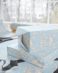 Light blue wrapping paper with a vintage carousel pattern, shown wrapped around gift boxes on a table with scissors and ribbon near a window.