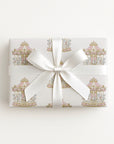 A rectangular gift box wrapped in white paper with a delicate pastel carousel pattern and tied with a wide white satin ribbon bow, photographed against a clean white background.