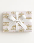 A rectangular gift box wrapped in pale pink wrapping paper with a repeating carousel pattern and tied with a wide white satin ribbon bow, shown on a clean white background.