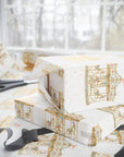White wrapping paper with a gold carousel illustration pattern, shown wrapped around gift boxes on a table with scissors and ribbon near a window.