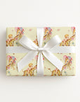 Gift wrapped with vintage baby and giraffe design with white ribbon on a yellow background.