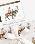 Vintage-style baby's first Christmas card with a baby hugging a reindeer and matching reindeer gift wrap, tied with white satin ribbon