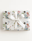 Flat lay of a gift wrapped in vintage-style snowman baby boy Christmas wrapping paper with a blue baby carriage and a white satin bow