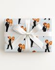 Gift wrapped in vintage bride and groom wrapping paper featuring a playful newlywed couple on pale blue, finished with a white satin bow.