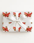 Wrapped gift in vintage-inspired airplane wrapping paper featuring a little boy flying a red biplane over a delicate navigation map with gold accents on an ivory background, tied with a white satin bow.