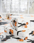 Funny white wrapping paper with a repeating illustration of a bride and groom, shown wrapped around gift boxes on a table with scissors and ribbon near a bright window.