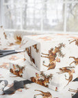 Christmas baby shower wrapping paper with baby riding a reindeer
shown wrapped around gift boxes on a table with scissors and ribbon nearby.