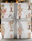 Close up of a gift wrapped in vintage-style pink nutcracker Christmas wrapping paper with a gray satin ribbon and glowing holiday lights behind