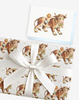 Vintage-style cowboy baby boy greeting card with a baby riding a farm bull, shown with matching gift wrap tied with a white satin bow