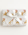 Vintage-style giraffe baby boy wrapping paper on a gift tied with a satin bow, baby boys riding giraffes in floral bonnets