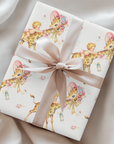 Gift wrapped in giraffe baby shower wrapping paper with a blush satin ribbon on soft cream fabric, baby girls riding giraffes in floral bonnets