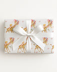 Vintage-style giraffe baby girl wrapping paper on a gift tied with a satin bow, baby girls riding giraffes in floral bonnets