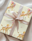 Gift wrapped in giraffe baby shower wrapping paper with a blush satin ribbon on soft ivory fabric, baby boys riding giraffes in floral bonnets