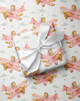 Flat lay of baby girl airplane wrapping paper with a wrapped gift tied with a white satin ribbon.