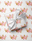 Wrapped gift tied with a white satin bow, displayed on matching wrapping paper featuring a little girl flying a pastel pink biplane over a delicate navigation map with gold accents on an ivory background.