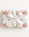 Wrapped gift in vintage-inspired airplane wrapping paper featuring a little girl flying a pastel pink biplane over a delicate navigation map with gold accents on an ivory background, tied with a white satin bow.
