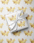 Wrapped gift tied with a white satin bow, displayed on matching wrapping paper featuring a little girl flying a pale yellow biplane over a delicate navigation map with gold accents on an ivory background.