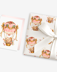New baby girl card with a baby in a pink floral hot air balloon beside matching pink hot air balloon baby shower wrapping paper tied with a ribbon
