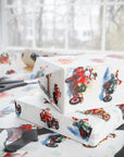 Stacked Christmas gifts wrapped in vintage-style snowman race car wrapping paper on a wrapping table with scissors and black ribbon