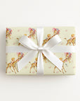 Vintage-style safari giraffe baby boy wrapping paper on a gift tied with a white satin bow, baby boys riding giraffes in floral bonnets on butter yellow