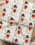 A gift-wrapped package wrapped in ivory holiday paper with a repeating snowman pattern, tied with a twine bow, placed on top of kraft paper envelopes.