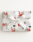 Flat lay of a gift wrapped in vintage-style Santa and snowman tennis Christmas wrapping paper with a white satin bow