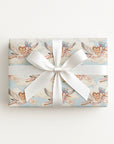 Flat lay of a gift wrapped in vintage-style twin baby shower wrapping paper with storks and a white satin bow