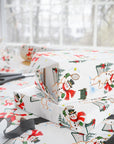 Stacked Christmas gifts wrapped in vintage-style Santa and snowman tennis wrapping paper on a wrapping table with scissors and black ribbon