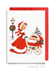 Vintage-style triplets first Christmas card: a woman in a red coat trimmed with white fur pushes a pram with three sleepy babies past a wreath-trimmed lamppost, shown with a red envelope, Winter Wonderland triplets baby shower card