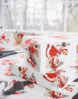 Flat lay of gifts wrapped in vintage-style triplets first Christmas wrapping paper with a woman in a red coat trimmed with white fur pushing a pram with three sleepy babies, with scissors and black ribbon nearby, Winter Wonderland triplets baby shower gift wrap