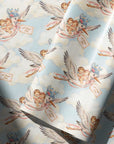 Vintage-style twin baby shower wrapping paper with a baby boy and girl riding a stork through soft blue clouds, shown as a roll in soft light