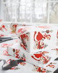 Flat lay of gifts wrapped in vintage-style twins first Christmas wrapping paper with a woman in a red coat trimmed with white fur pushing a pram with two sleepy babies, with scissors and black ribbon nearby, Double the Joy twin baby shower gift wrap