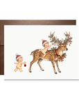 Vintage-style Christmas card with two babies in Santa hats, one riding a spotted reindeer with holly and ornaments on its antlers.
