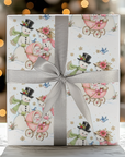 Gift wrapped in vintage-style snowman baby girl Christmas wrapping paper with a pink baby carriage and a gray satin ribbon, glowing holiday lights behind