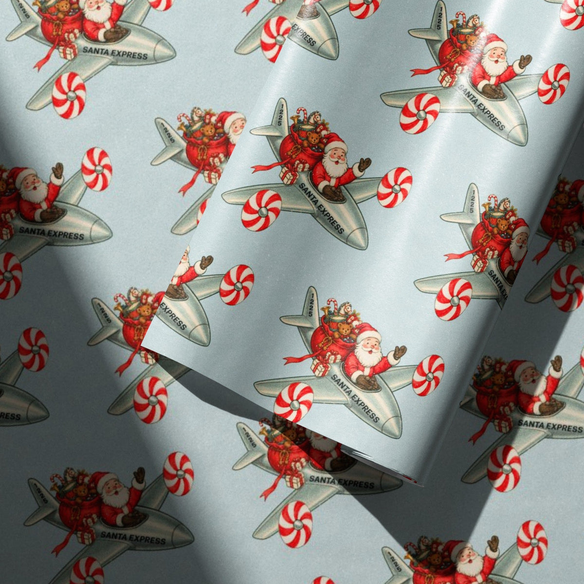 Light blue wrapping paper with a repeating pattern of Santa Claus in a silver Santa Express airplane, surrounded by red and white peppermint candies.