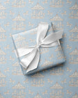 A square gift box wrapped in light blue wrapping paper with a repeating carousel pattern, tied with a white satin ribbon, placed on top of the same patterned paper.