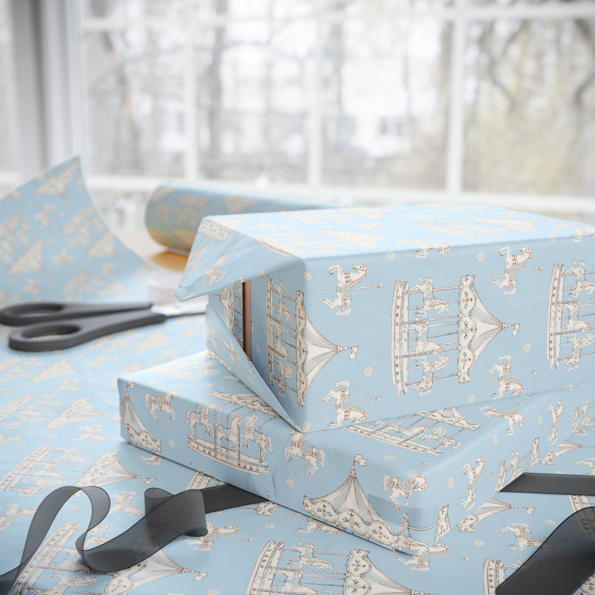 Light blue wrapping paper with a vintage carousel pattern, shown wrapped around gift boxes on a table with scissors and ribbon near a window.