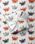 A wrapped gift box tied with a white satin ribbon, placed on top of wrapping paper printed with a repeating pattern of vintage red, blue, and gold biplanes on a white background.