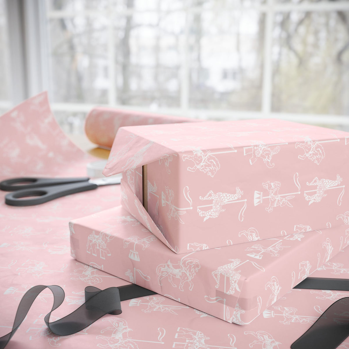 Pink wrapping paper with a white carousel horse pattern, shown wrapped around two gift boxes on a table with scissors and ribbon near a window.