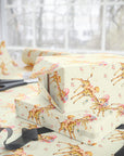 Yellow baby-themed wrapping paper with giraffes and little girls, shown wrapped around gift boxes on a table with scissors and ribbon near a bright window.