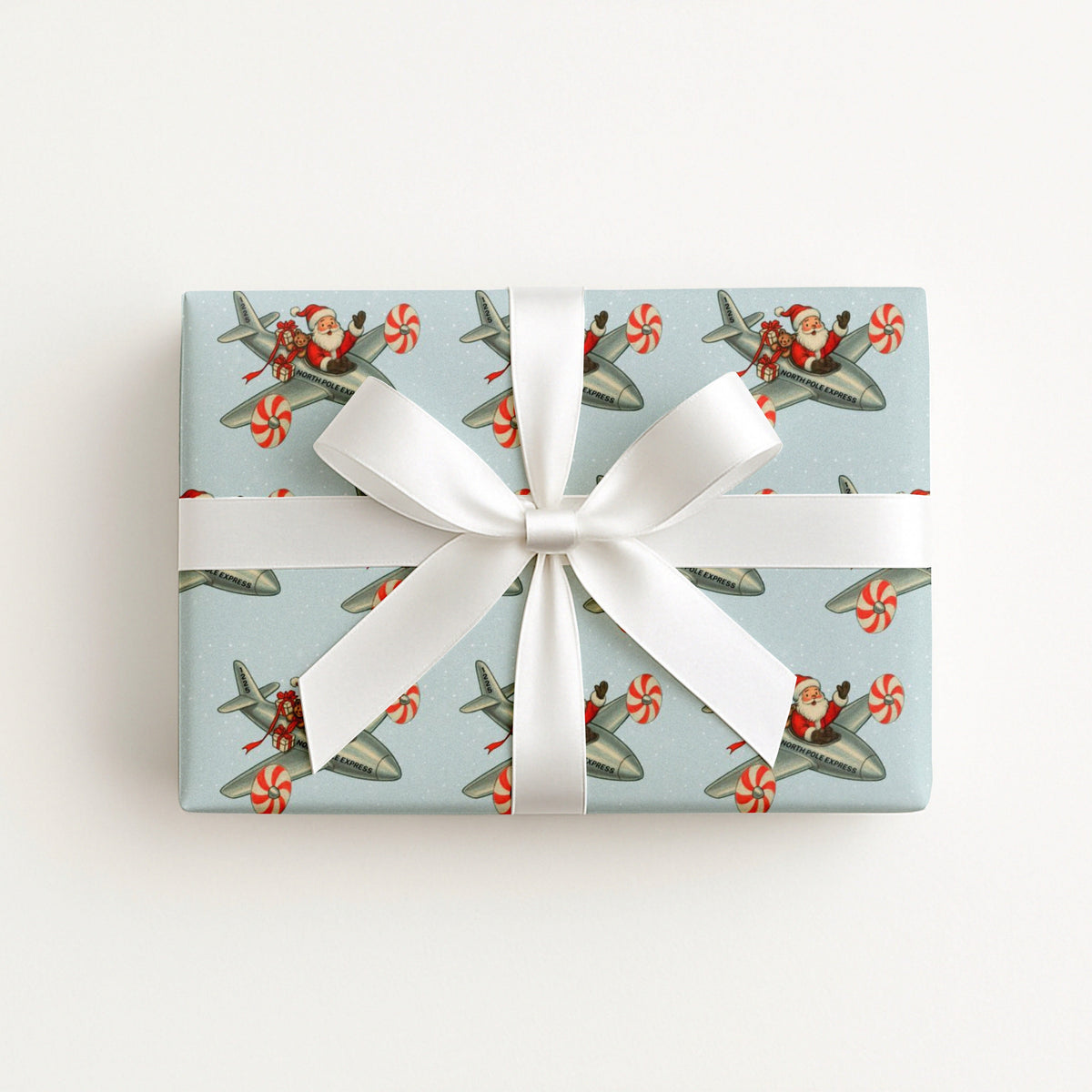 A rectangular gift box wrapped in a vintage-inspired Christmas wrapping paper featuring Santa flying a silver airplane with peppermint striped propellers on a light blue background.