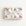 A rectangular gift box wrapped in ivory wrapping paper with a repeating pattern of vintage pink airplanes with shark mouth noses and gold accents, tied with a wide white satin ribbon and bow, on a plain white background.