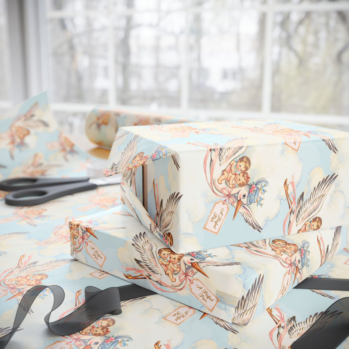 Stacked baby shower gifts wrapped in vintage-style twin stork wrapping paper on a wrapping table with scissors and black ribbon