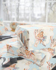Stacked baby shower gifts wrapped in vintage-style twin stork wrapping paper on a wrapping table with scissors and black ribbon