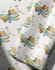 Vintage-style wedding wrapping paper with a bride and groom kissing in a blue biplane, surrounded by clouds, tiny stars and pink flower bouquets.