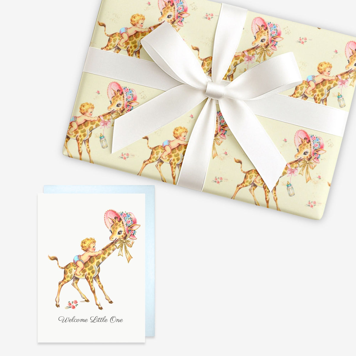 Giraffe baby shower wrapping paper on a gift tied with a satin bow beside a matching Welcome Little One greeting card