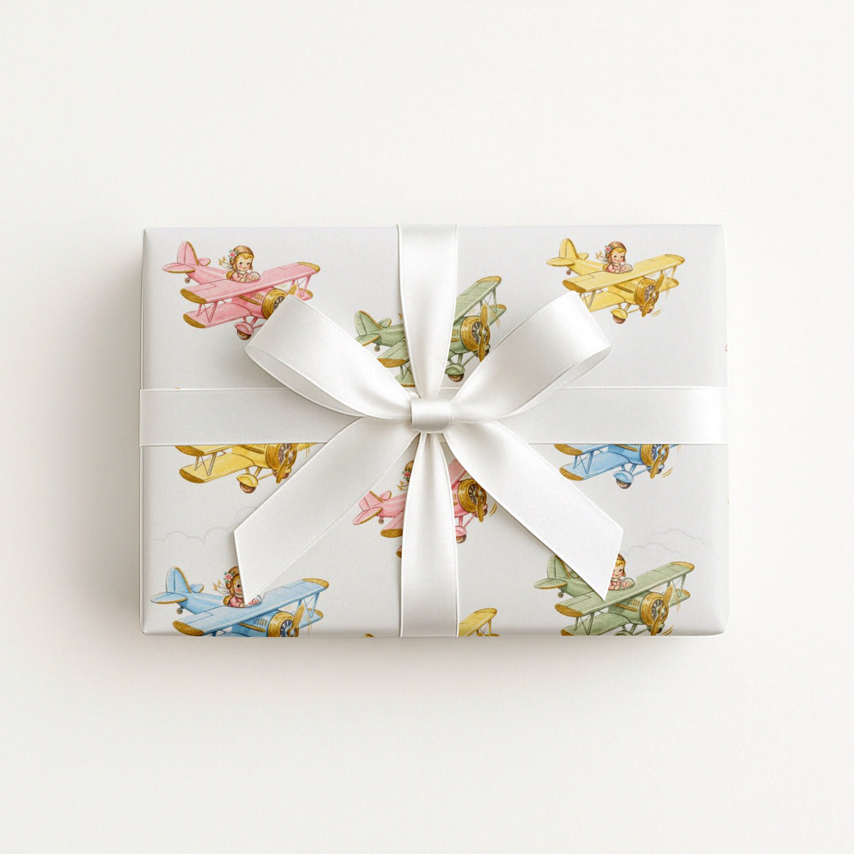 Gift box wrapped in a a decorative paper featuring biplanes in pastels on a light background