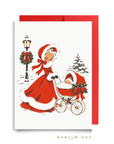 Vintage-style baby's first Christmas card: a woman in a red coat trimmed with white fur pushes a pram with one sleepy baby past a wreath-trimmed lamppost, shown with a red envelope, Baby It's Cold Outside baby shower card