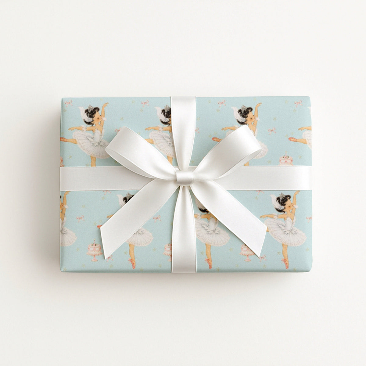 A rectangular gift box wrapped in light aqua wrapping paper featuring a ballet dancer pattern, tied with a wide white satin ribbon and bow, photographed from above on a clean white background.