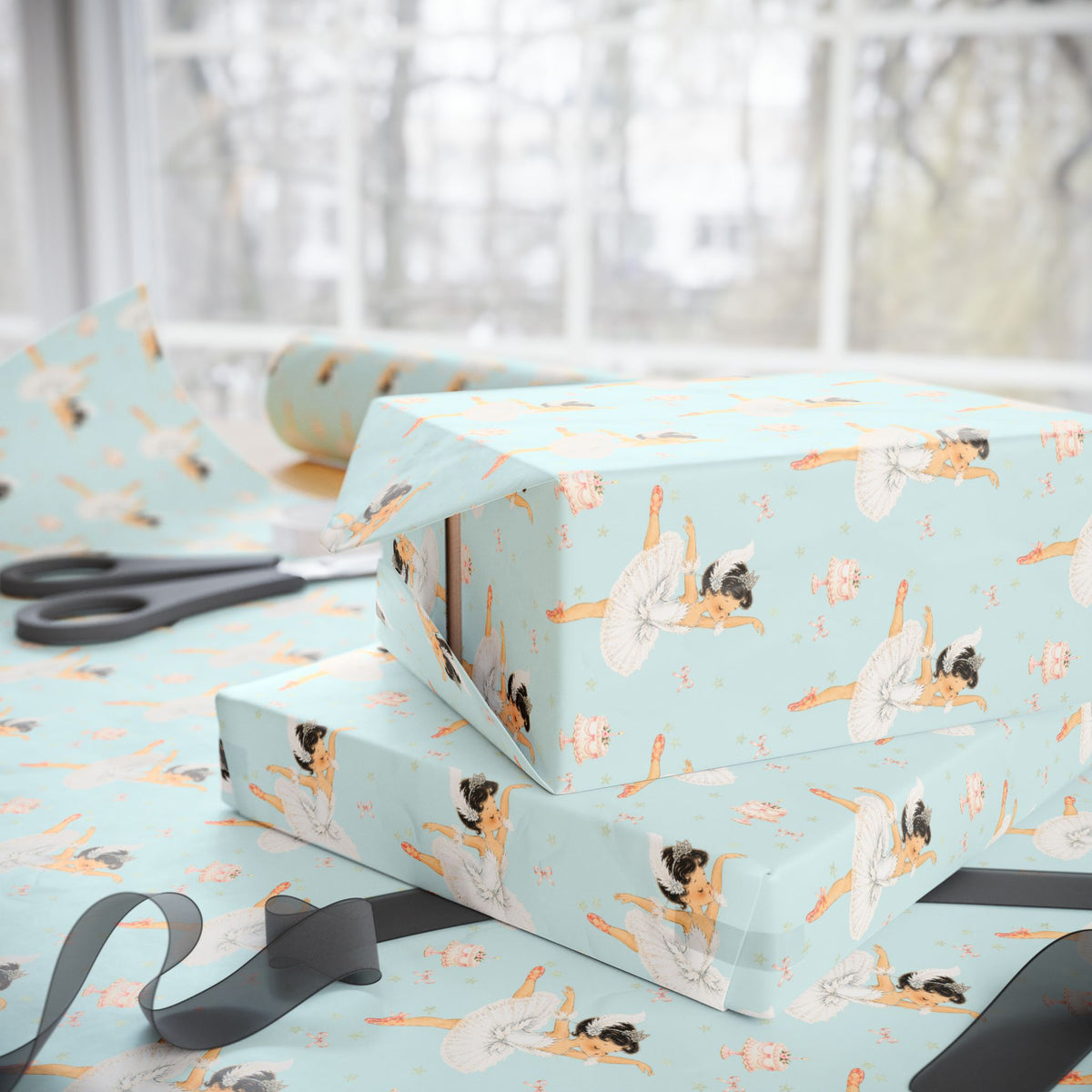 Light aqua wrapping paper with a darling girl ballet dancer pattern, shown wrapped around gift boxes on a table near a window, with scissors and ribbon visible.